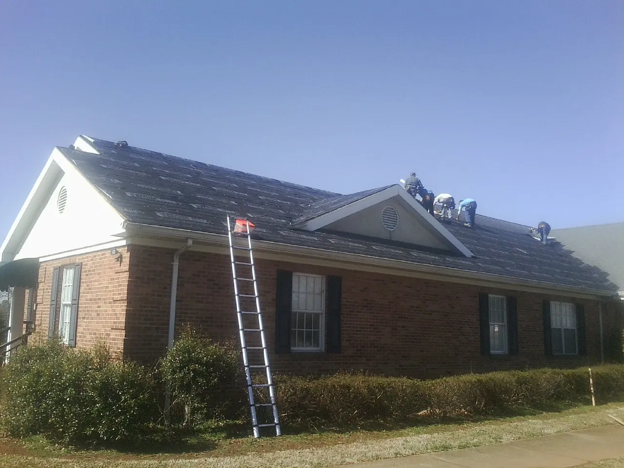 Crew tearing shingles off a brick ranch roof with a ladder set — Emergency Roof Repair work by our crew in Hope