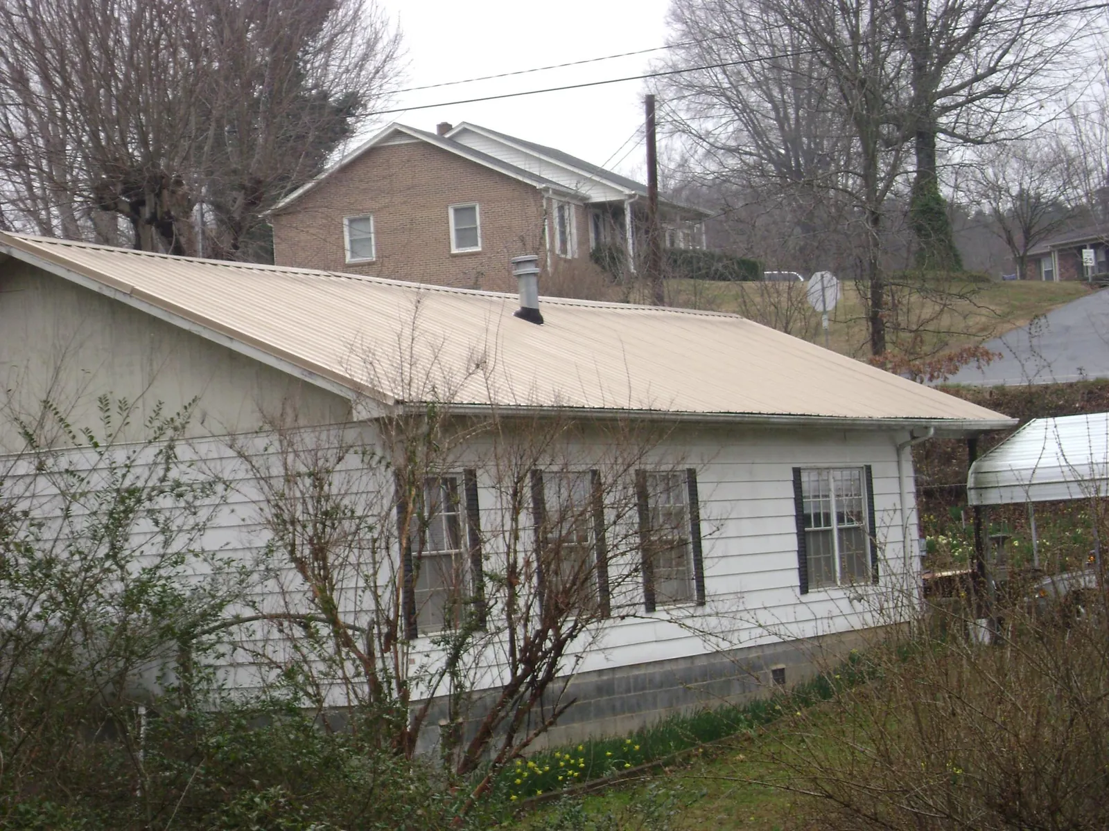 Tan metal roof on a white sided house set into a hillside — Commercial Roofing by Roofing Brothers in Hope